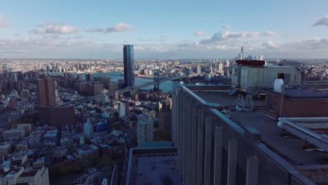 Forwards-fly-around-top-of-high-rise-building.-Revealing-view-of-pair-of-bridges-connecting-Manhattan-and-Brooklyn.-Manhattan,-New-York-City,-USA