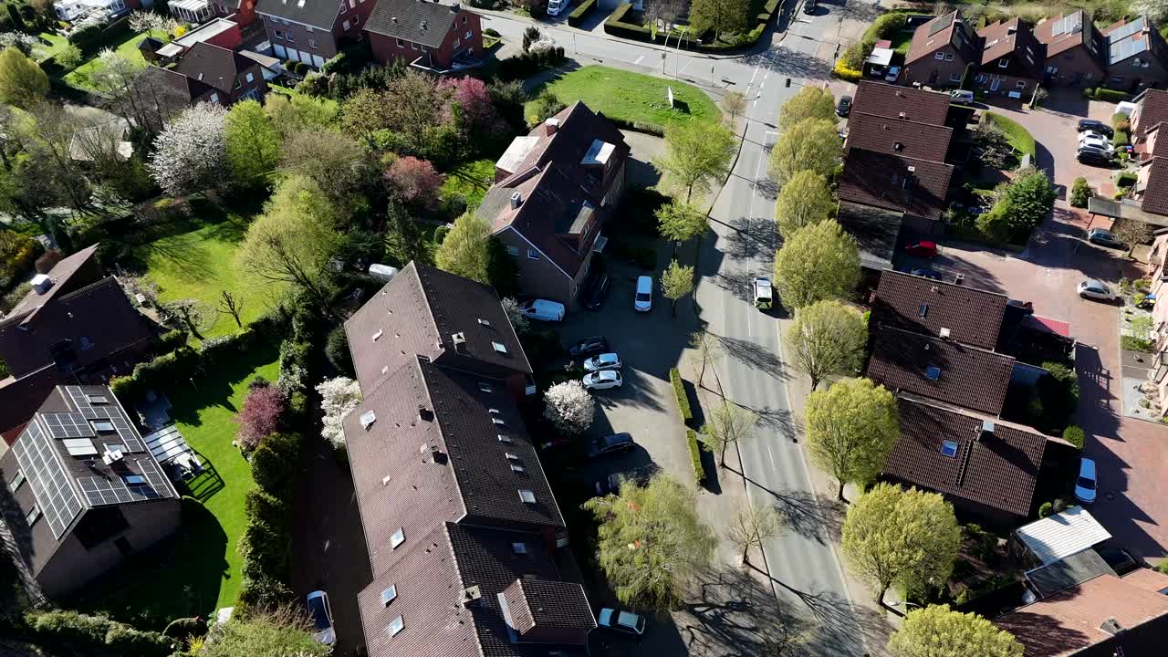 German police car on street during sunny day. Aerial top down shot. Row of houses and homes along green blooming trees in spring. Tracking shot.