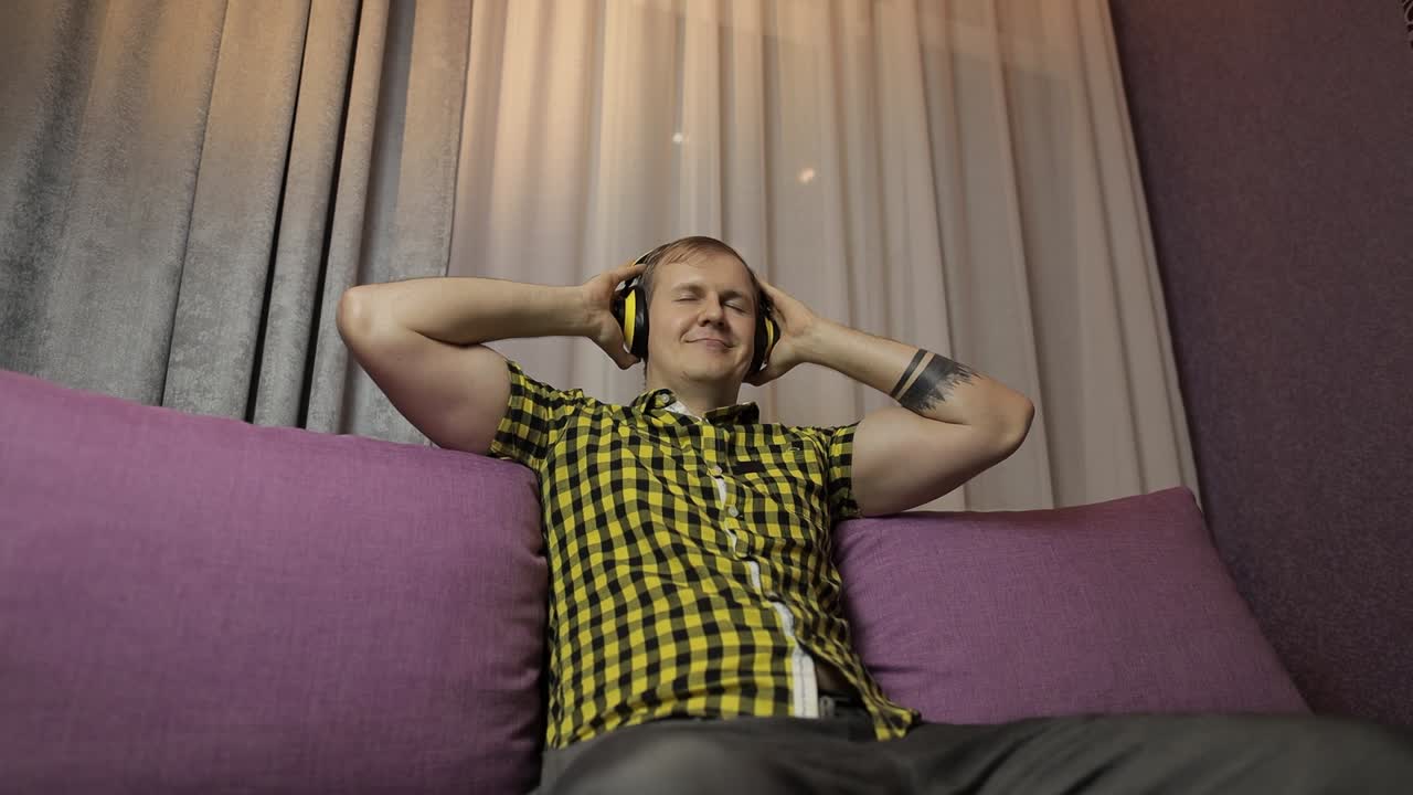 소파에 앉아 무선 헤드폰으로 음악을 듣고 춤을 추는 남자