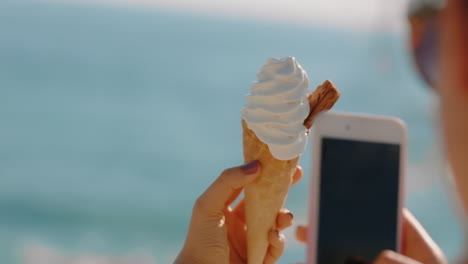 mujer de mano cercana tomando una foto de helado usando un teléfono inteligente disfrutando de las vacaciones de verano comiendo servicio suave en la playa compartiendo experiencia