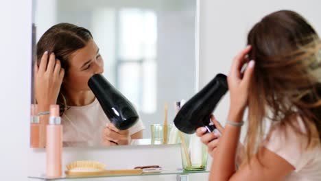 beauty and people concept  teenage girl with hair dryer looking to mirror at home bathroom