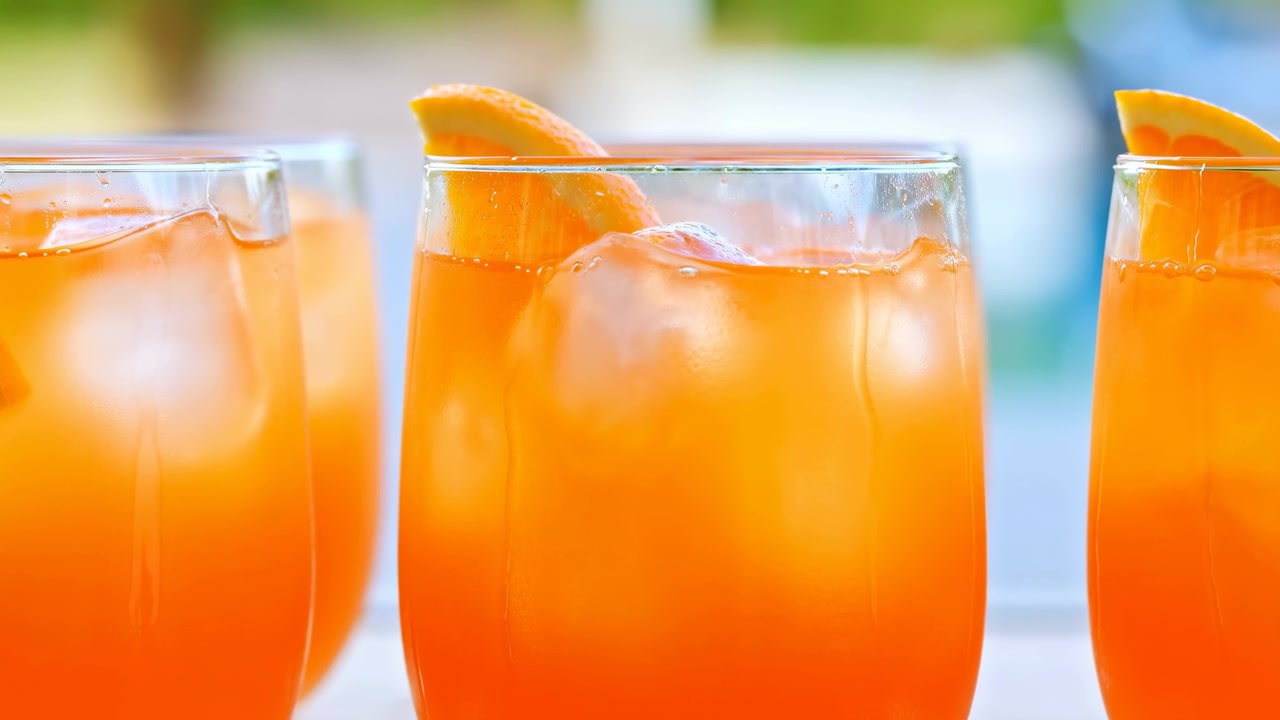 Cocktail arancioni brillanti con ghiaccio, bicchieri da piscina illuminati dal sole guarniti con fette d'arancia, condensa su vetro trasparente.