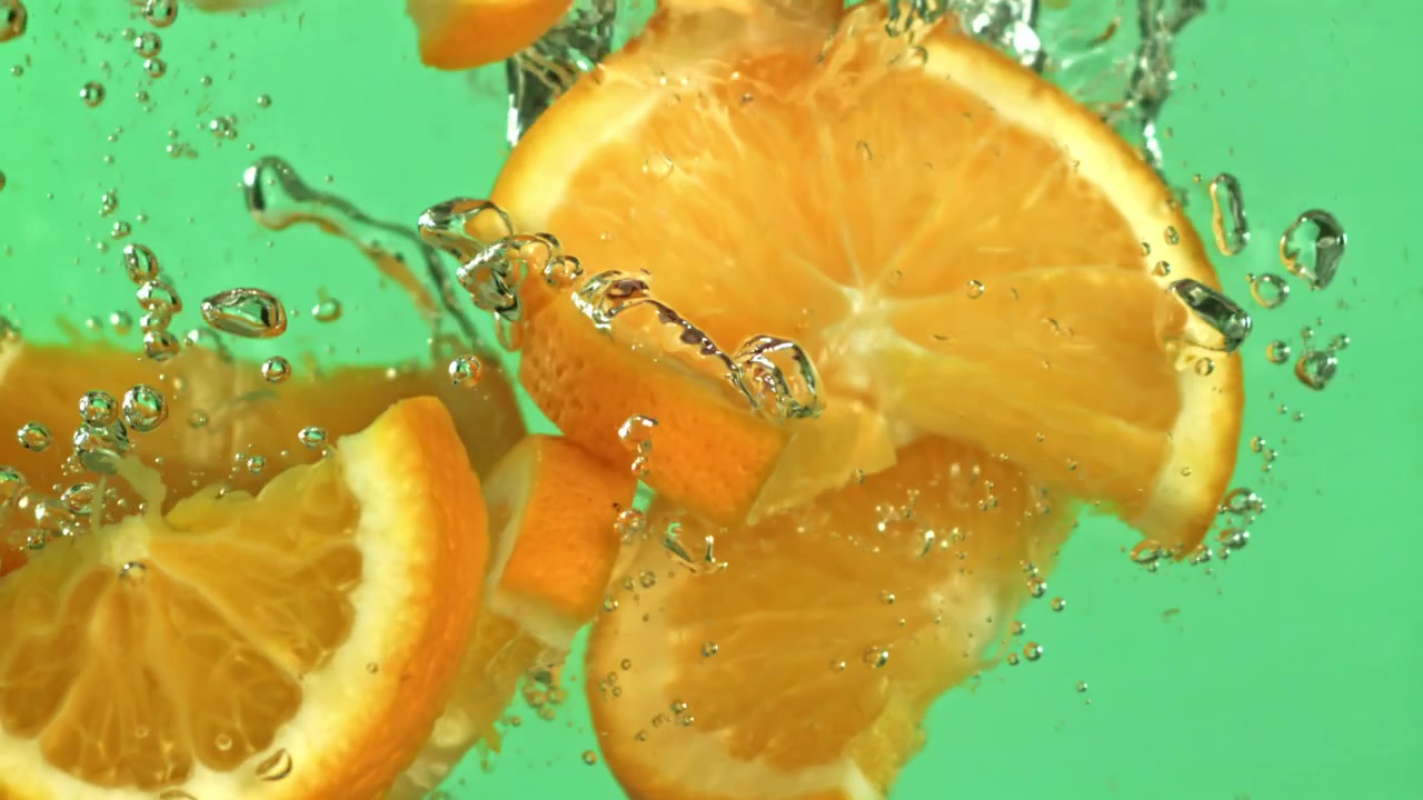 Fette d'arancia che cadono al rallentatore nell'acqua con bolle.