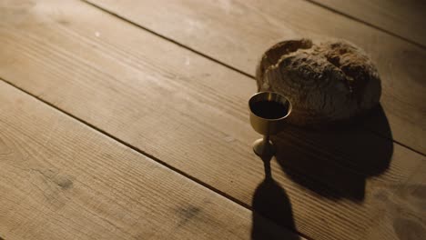 concepto religioso filmado con pan de cáliz y vino en una mesa de madera con un charco de luz 5