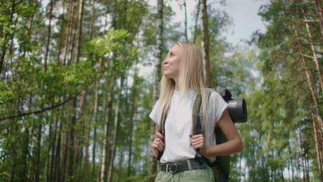 Caucasian-blonde-Woman-exploring-glade-with-ferns-in-the-woods.-hiking-woman-walk-in-rainforest-jungle.-Girl-hiker-walking-with-backpack-through-dense-rain-forest-nature