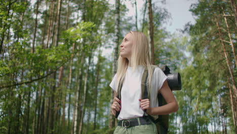 caucasian blonde woman exploring glade with ferns in the woods. hiking woman walk in rainforest jungle. girl hiker walking with backpack through dense rain forest nature