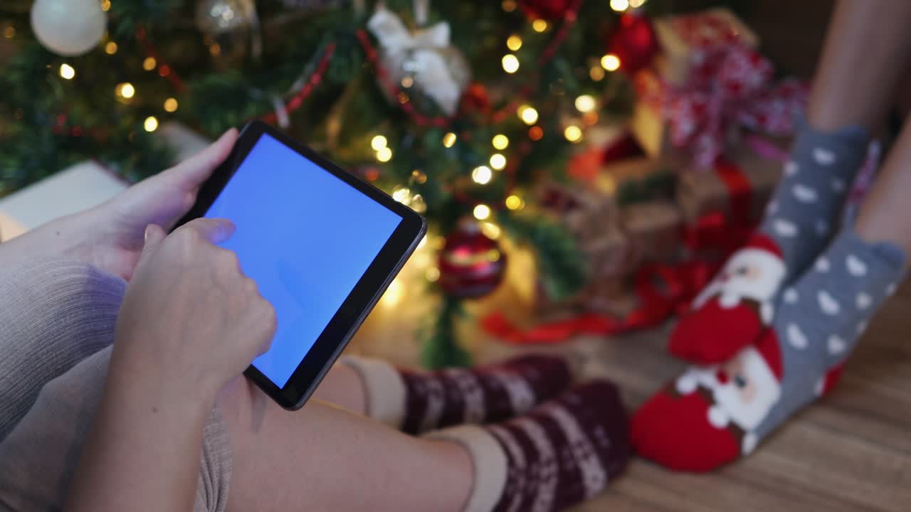 woman in Christmas warm socks sitting under decorated fir tree tablet chromakey