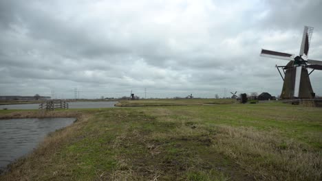 Dutch-windmills-turning-in-wetlands,-camera-pan-reveal