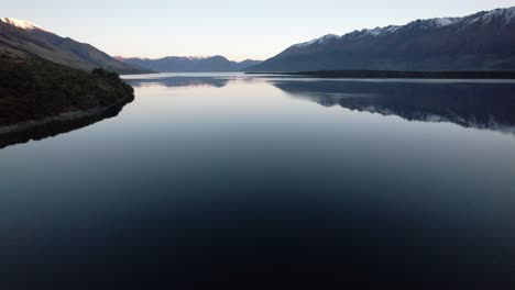 Aerial-flying-over-Lake-Wakatipu-with-the-lake-surrounded-by-snow-capped-mountains-reflecting-in-the-lake-just-after-sunset-in-Queenstown-New-Zealand