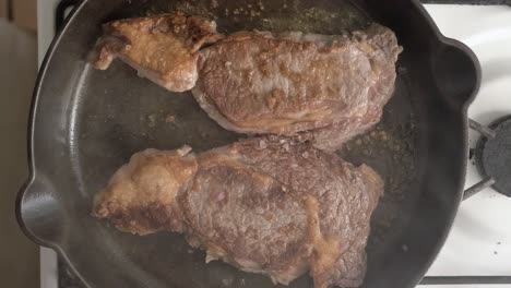 steaks fried and flipped in a cast iron skillet with oil - overhead view