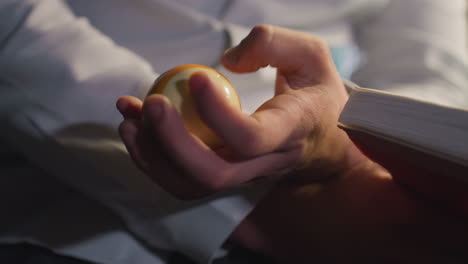 close-up shot of hand in white shirt, face not visible, holding an open book while rolling a billiard ball in one hand. focused gesture, moody lighting, and intense concentration