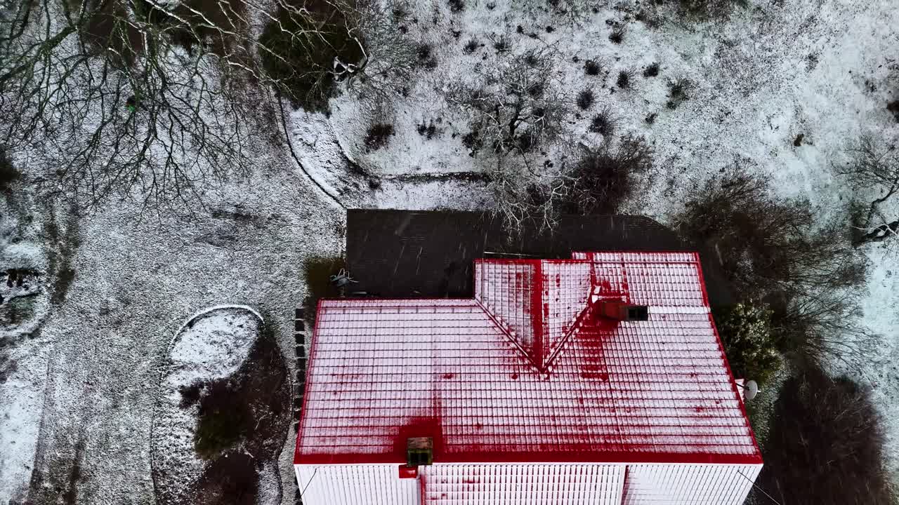 Aerial view of a snow-covered building with a red roof surrounded by a winter landscape, captured by drone