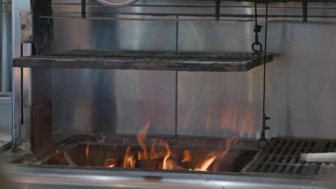 A wood fired open flame grill heating up with the pulley system holding up the grill plate allowing access to the fire in a commercial kicthen