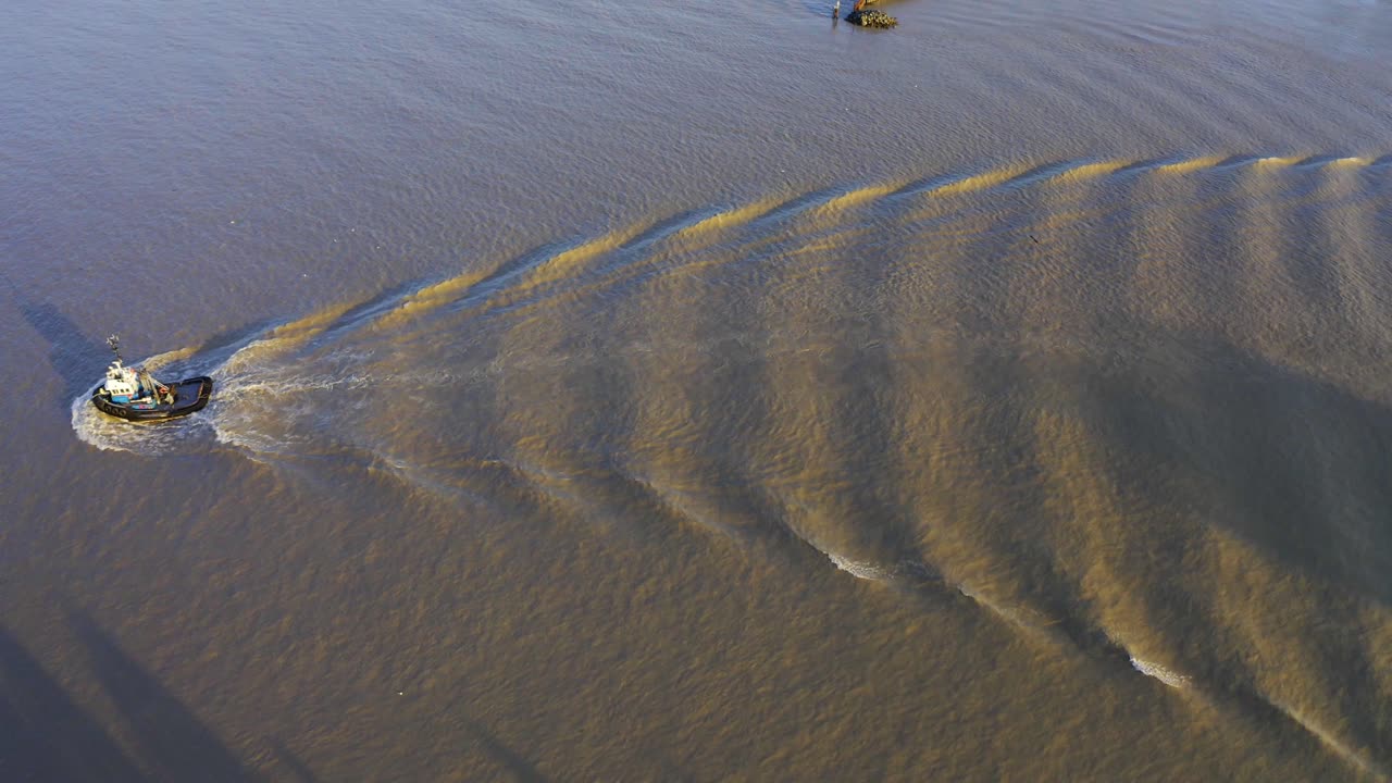 상업 강을 지나가는 공중 조감도 예인선은 황혼의 일몰에 파도를 일으키고 물에 반사되는 진흙 투성이의 물 반사는 상업 직진 보트에 그림자가 드리워져 경로에서 작업을 합니다.