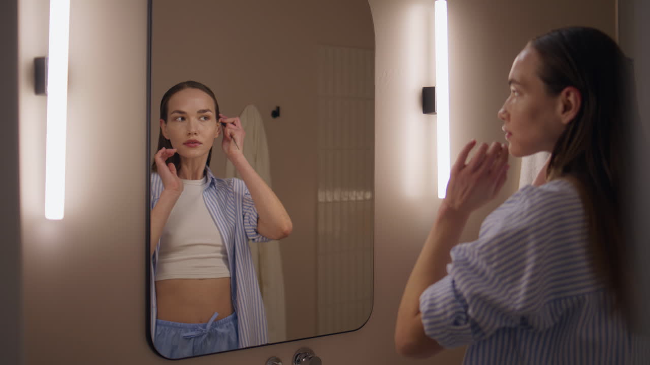 Girl reflection combing hair in soft bathroom light. Attractive woman styling