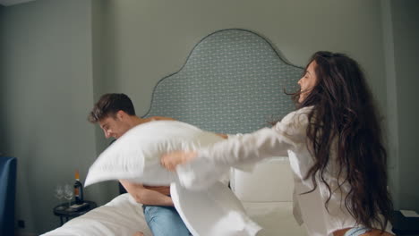 Pareja-Sonriéndose-En-La-Habitación-Del-Hotel.-Pareja-Alegre-Jugando-Almohadas-En-La-Cama.