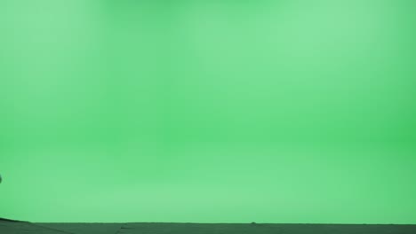 green screen chroma key studio: beautiful young woman wearing stylish turtleneck and backpack holding mobile phone smartphone walks happily across room left to right. side view camera shot