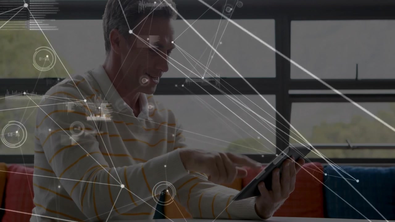 Man sitting on sofa holding tablet looking down updating data network overlays exploring insights