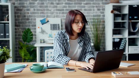 slow motion of pretty girl working in office using laptop typing sitting at desk