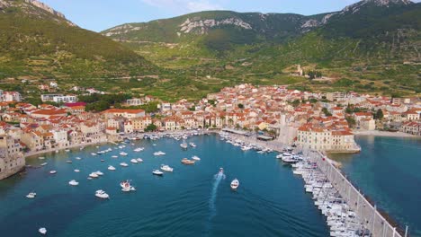 Panorama-Einer-Küstenstadt-Mit-Vielen-Häusern-Mit-Roten-Dächern,-Umgeben-Von-Meer-Und-Bergen-Mit-Yachten-In-Der-Marina-Bay-Und-Glockenturm-Und-Pier