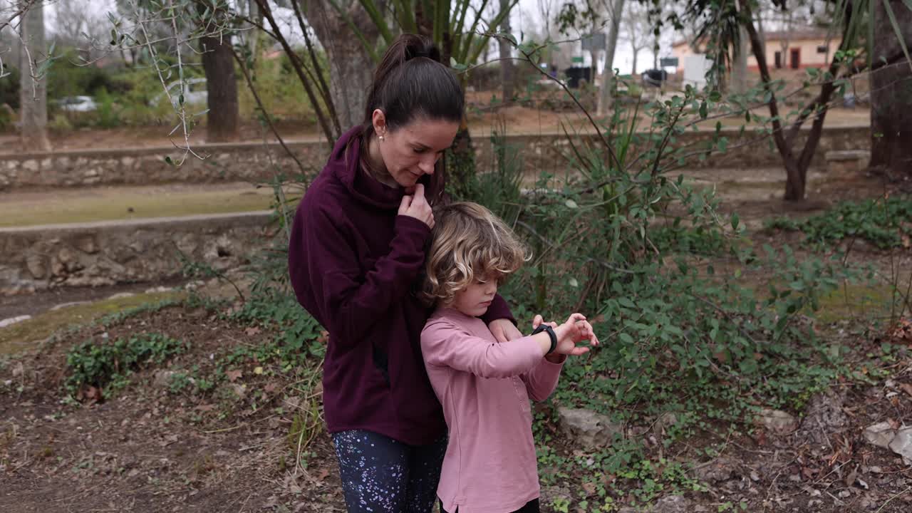 mamá explicando a su hijo cómo usar un reloj de pulsera al aire libre