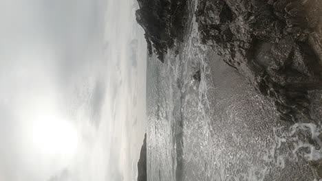 VERTICAL-slow-motion-ocean-waves-crashing-against-rock-sandy-beach-coastline-at-sunrise