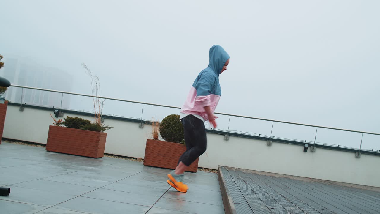 Sport woman in sportswear wears hood doing workout step cardio exercising training on roof of house