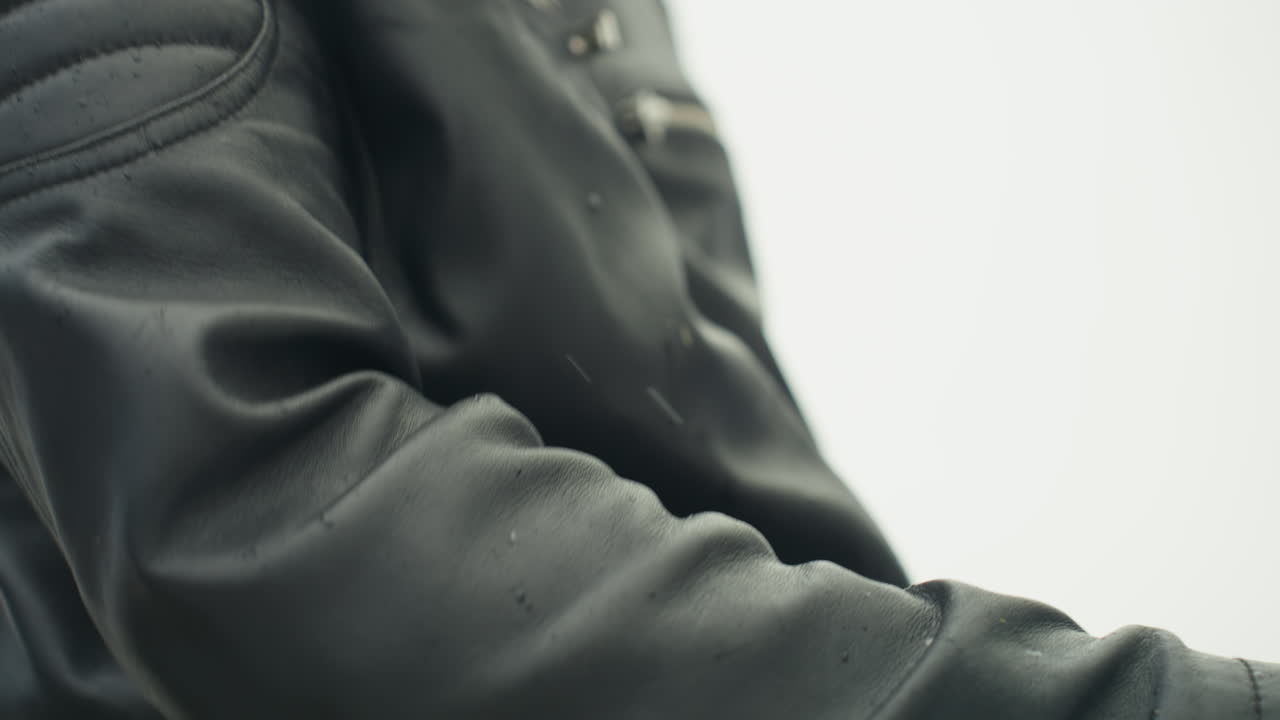 Detailed shot of perspiring leather sleeve with droplets and rider gear. Macro view of water droplets on leather jacket sleeve demonstrating outdoor riding attire and textured grain