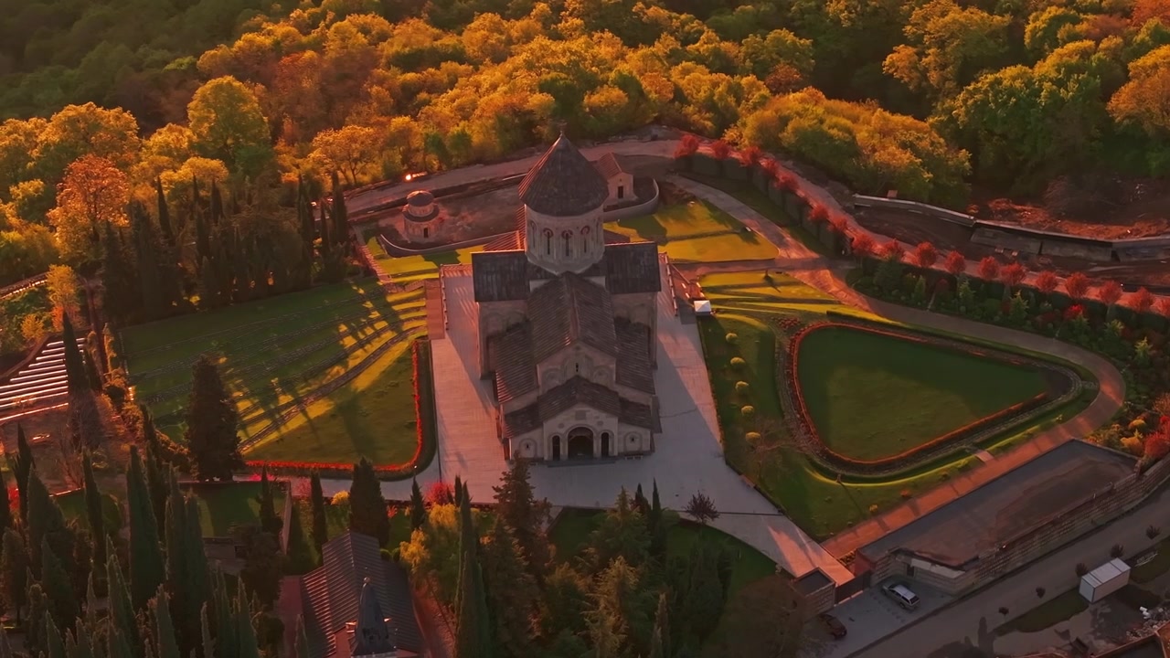 Aerial drone view of Gelati Monastery in Georgia at sunrise, with warm golden hour light illuminating the historic complex and surrounding landscape from above.