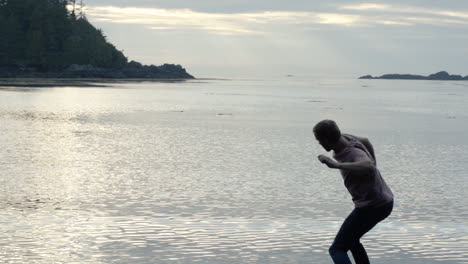 slow motion man skipping rock on ocean beach and sunset