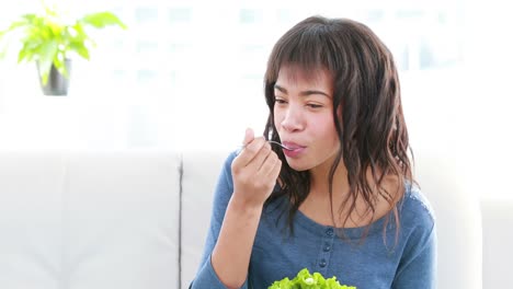 Fröhliche-Hübsche-Frau,-Die-Gesunden-Salat-Isst-Und-Auf-Dem-Sofa-Sitzt