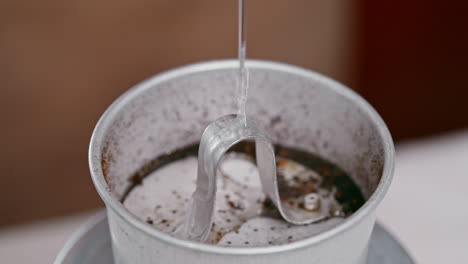 a close-up view of slowly poured boiling water into a vietnamese coffee phin