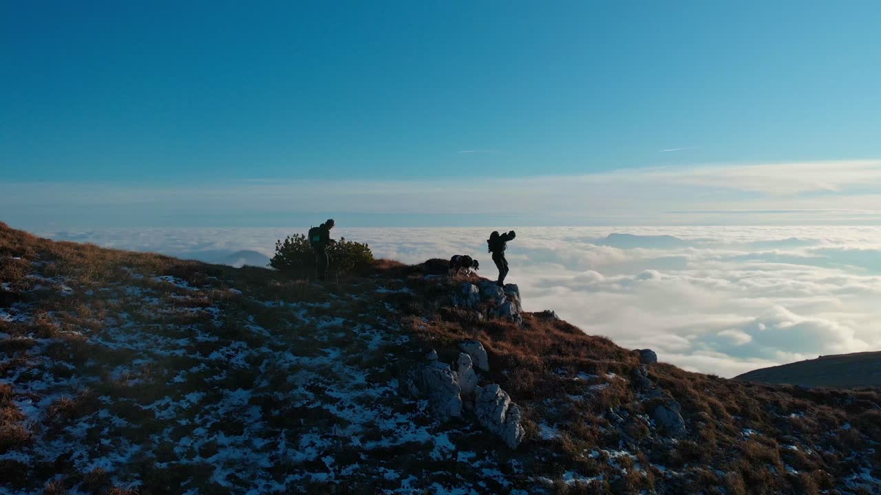 seguendo due ragazzi e un cane che camminano sulla cresta di una montagna, un mare di nuvole si allunga all'orizzonte