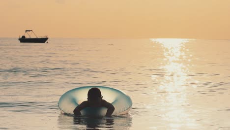 little boy swimming in water lying on rubber ring on summer vacations at sea