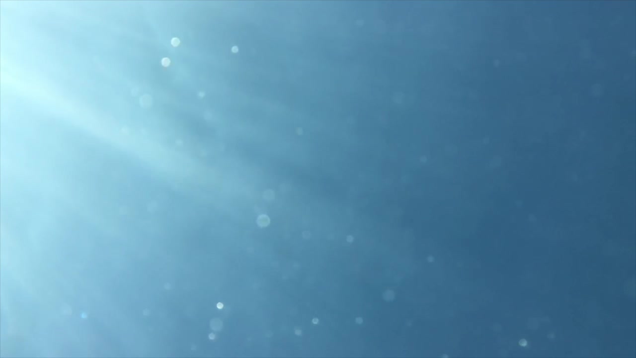 Bubbles floating in the water in slow motion with a few light rays coming in from the left