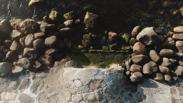Luftfoto af vand, der strømmer fra en stenet flod dækket af mos.