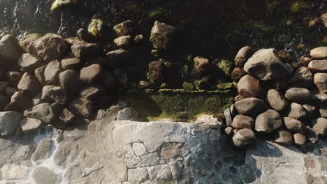 bird's eye view shot of water streaming from a rocky river covered in moss