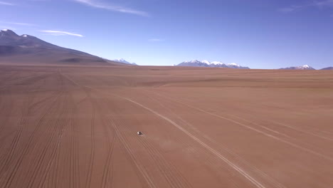 Aerial-rotating-drone-shot-of-car-in-a-desert-in-Eduardo-Avaroa-National-Park,-Bolivia