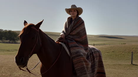 woman riding a horse in a field with a cowboy hat and blanket
