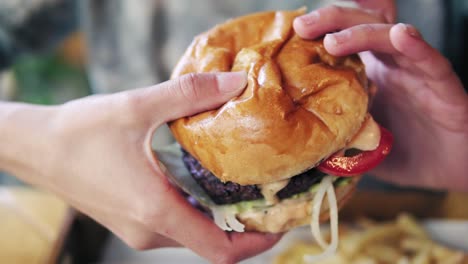 female hands taking big tasty burger from a wooden tray and getting ready to eat it. slow motion shot