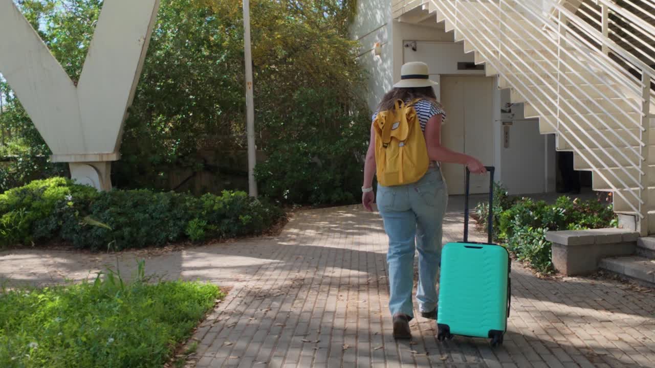 Een vrouw loopt met een groene koffer over een pad.