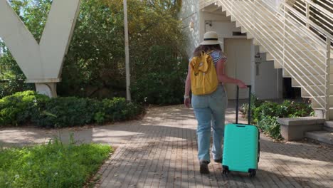 a woman is walking down a path with a green suitcase