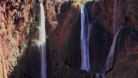 tourists look on as three waterfalls plunge down the sheer cliff walls in morocco