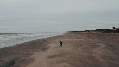 vista aérea de una persona vestida de negro montando una motocicleta en la arena