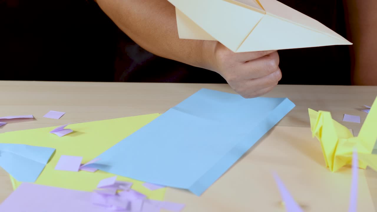 Hands fold a paper airplane on a colorful craft table under bright, even lighting