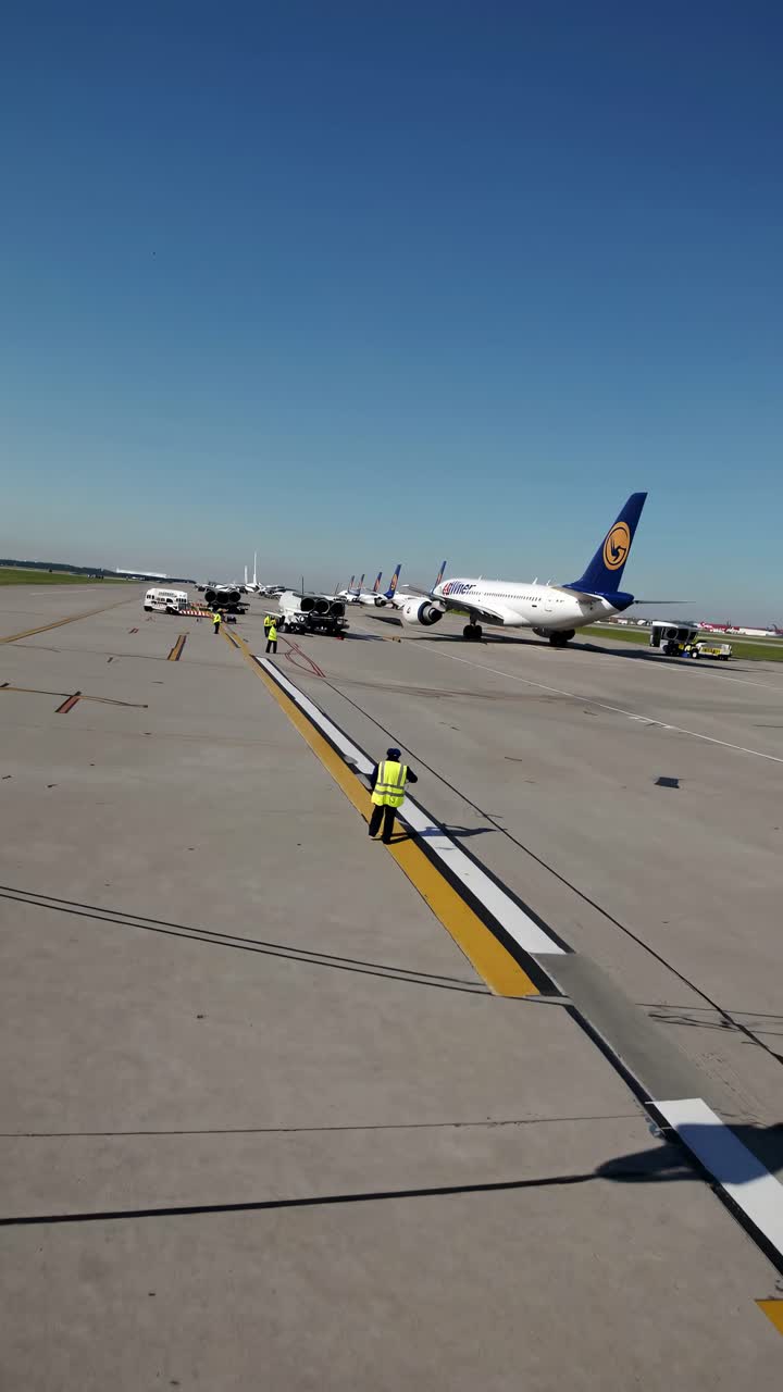 A ground-level view of an airport runway with planes and workers, capturing the busy atmosphere
