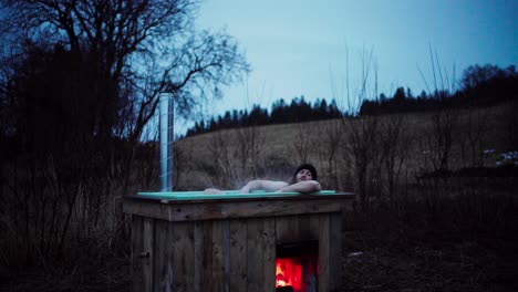 Hombre-Disfrutando-Del-Agua-Caliente-En-Un-Jacuzzi-De-Leña-En-La-Granja-Por-La-Noche