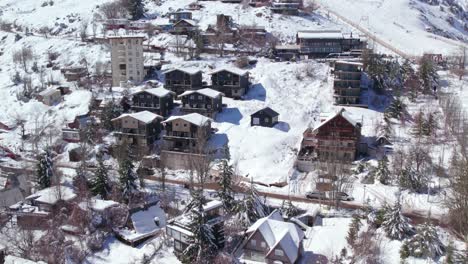 Vista-Aérea-Rodeando-Los-Farellones-Cubiertos-De-Nieve-En-La-Ladera-De-La-Colina-De-La-Estación-De-Esquí-Chalet-Y-Barrio-Hotelero-En-Santiago,-Chile.