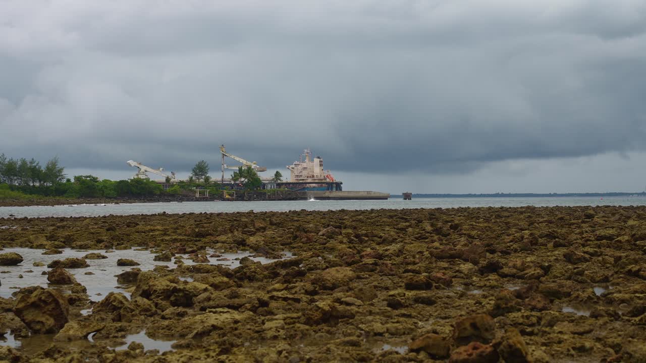 A shot of a power plant standing at the water’s edge, striped stacks and cranes framed by storm clouds of Mauban Port, Quezon Province Philippines