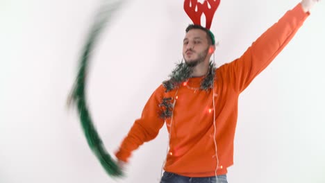 young happy man waving a green garland and dancing. man in christmas mood with red reindeer antlers